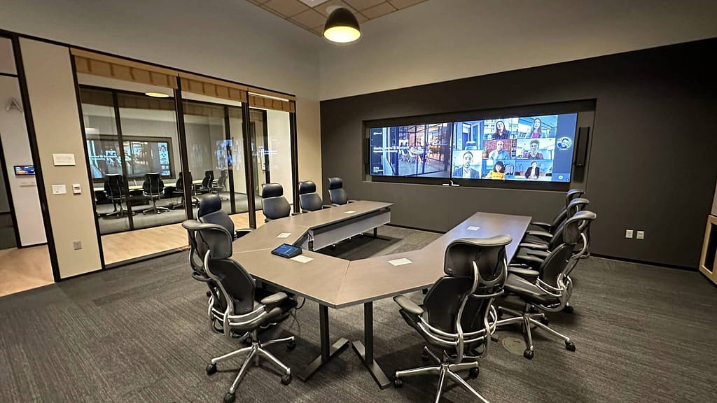 Microsoft Teams Room setup in a modern conference space with large wall-mounted display, integrated video conferencing system, and collaborative meeting table for seamless hybrid communication.